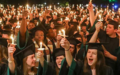 Students in Commencement attire holding candles at night and celebrating near the historic Wren Building at the annual Candlelight Ceremony