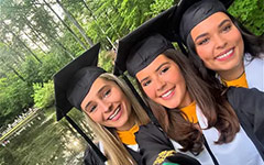 Three smiling graduates pose for a selfie on the Crim Dell bridge