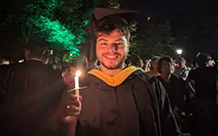 A smiling graduate poses with a candle during the Candlelight ceremony in the Wren Yard