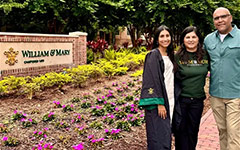 Two people pose with a graduate in Commencement attire near the William & Mary sign