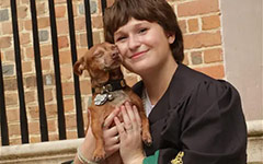A graduate and their small dog pose together on the steps of the Wren Building