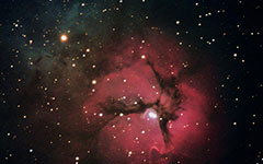 Trifid Nebula viewed through a telescope - The red region is an area of ionized hydrogen where stars are forming and the blue region is a cloud of dust particles that reflect the light from nearby stars