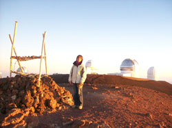 Francesca at the top of Mauna Kea, Hawaii. She is standing beside a traditional Hawaiian altar and behind her are some of the best telescopes in the world
