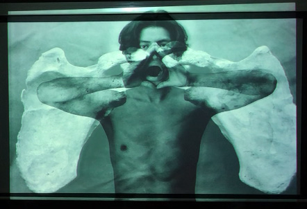 Slide 27: The fourth Angel. A shirtless young man poses with hands cupped around his mouth as if he is shouting. His image is imposed over the image of large scapula bones that extend over his shoulders like wings.