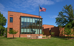 A brick building with large glass windows and an American flag on a flagpole