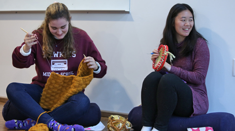 Two students sit on the floor and work on knitting
