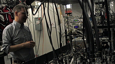 Seth Aubin, associate professor of physics at William & Mary, stands in front of a table of lenses, mirrors and other optics that his team uses to manipulate light to cool rubidium and potassium atoms. 