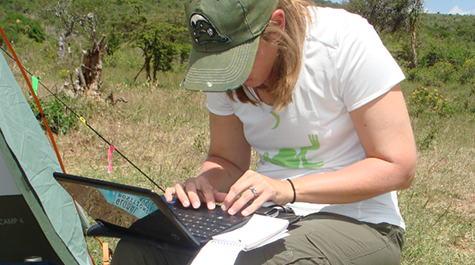 Carrie Dolan hunches over her computer taking notes in the field. 