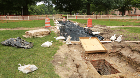A hole in the ground near a construction area shows a vaulted brick drain