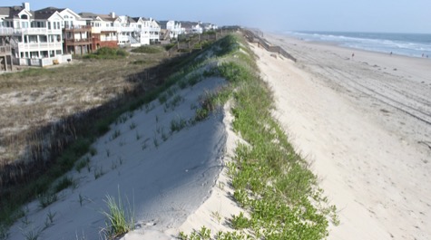 A sand dune with the beach visible on one side and houses on the other