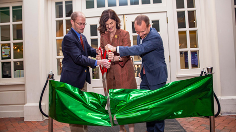 Three people use large scissors to cut a giant, green ribbon