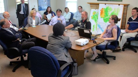 People sit around a conference room table with a map behind them