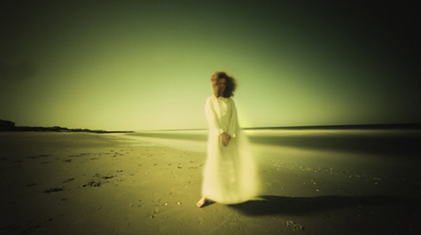 A person in a long, white gown stands on a beach