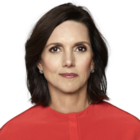 Beth Comstock wearing a red shirt and standing in front of a white backdrop