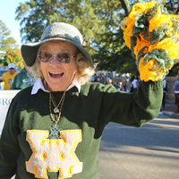 A person in a green W&M sweater waves a pompom in a parade