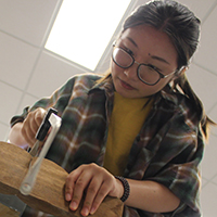 A William & Mary student saws a piece of wood for a sculpture design