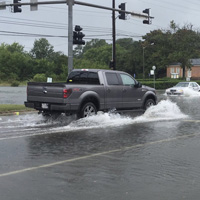A pickup truck drives through a flooded intersection, splashing water