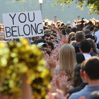 A sign saying "You Belong" is held up among a large crowd outside of the Wren Building