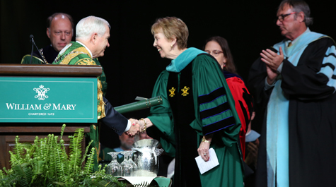 Susan Magill dressed in academic regalia shakes the hand of Robert Gates on a stage