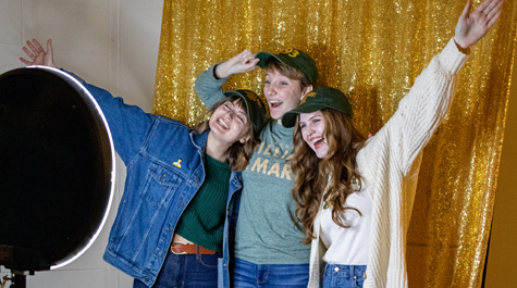 Three students pose in front of a gold background in a photo booth