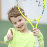 A child gives a thumbs-up while holding a tennis racket