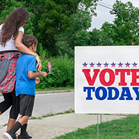 Woman and child walk past "vote" sign 