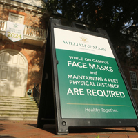 A sandwich board sign outside of the Wren Building says masks are required on campus
