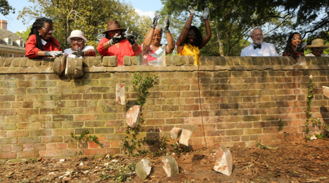 People push bricks off of the top of a brick wall