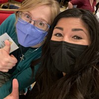 Two people wearing masks give a thumbs-up