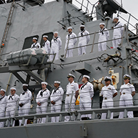 Sailors stand at the rails aboard a Navy ship