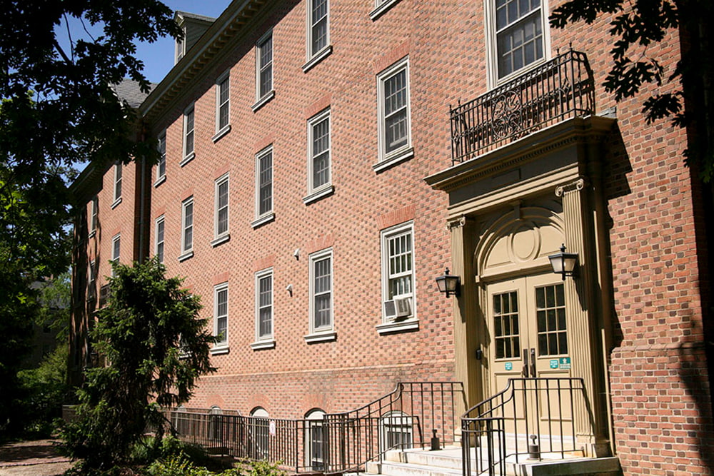 An entrance with stairs leads to a brick, windowed dorm building.
