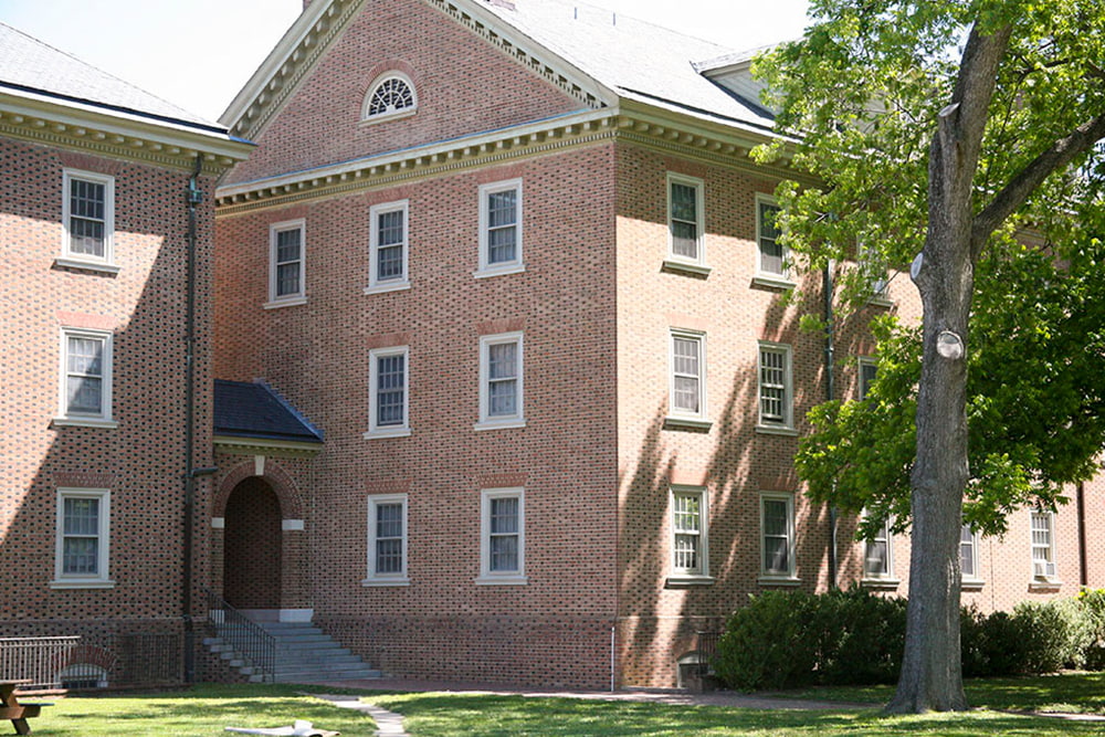 An entryway with stairs leading to a brick, windowed dorm building.