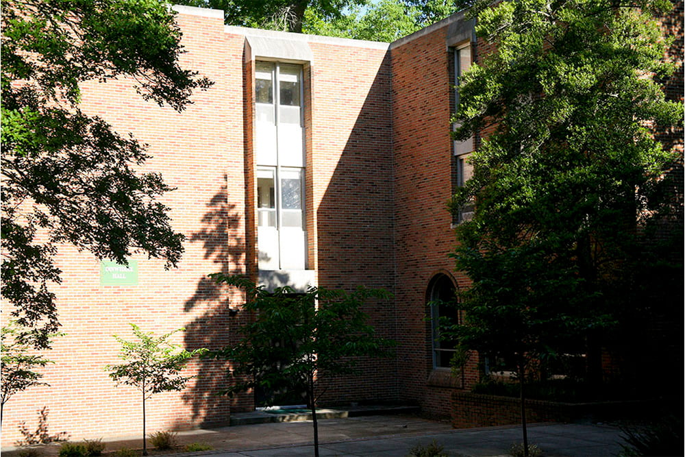 The sun casts a shadow over an entrance into a brick, windowed dorm building.