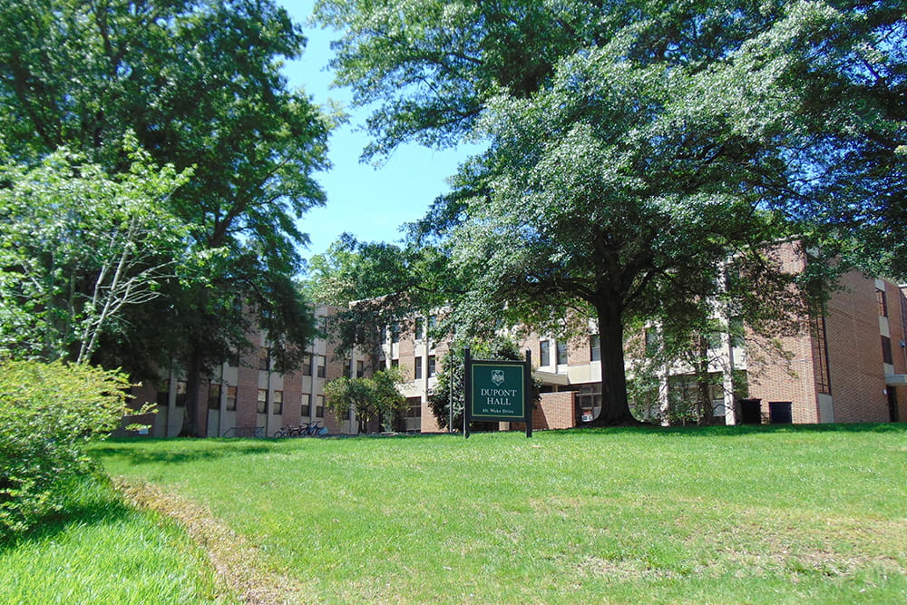 Brick, windowed dorm building nestled in greenery.