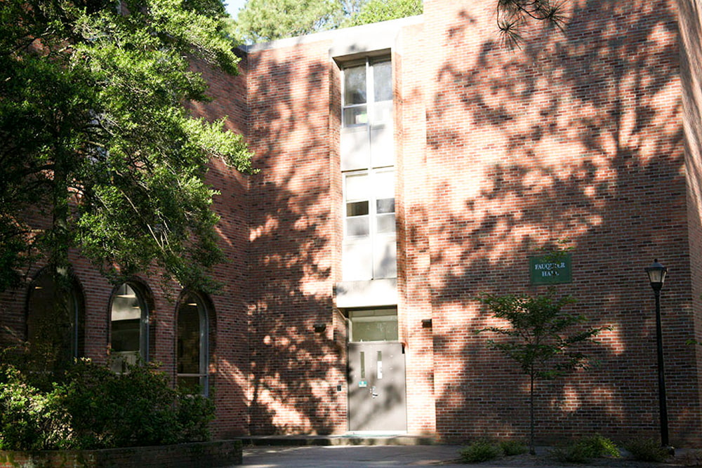 Three arched windows and an entrance to a brick, windowed dorm building.