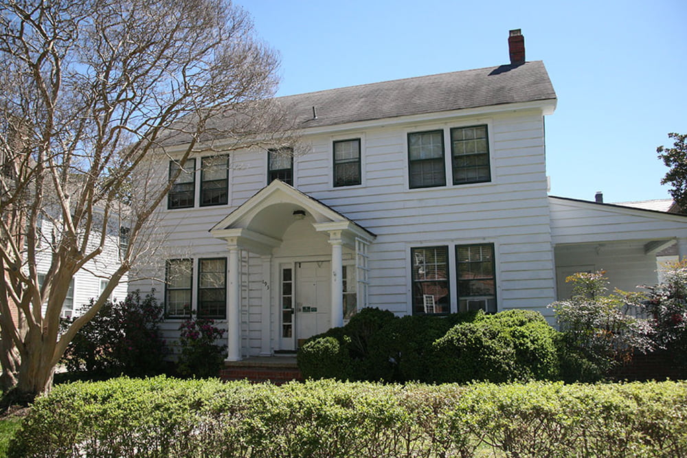 An historic house with side porch and white siding on a residential street