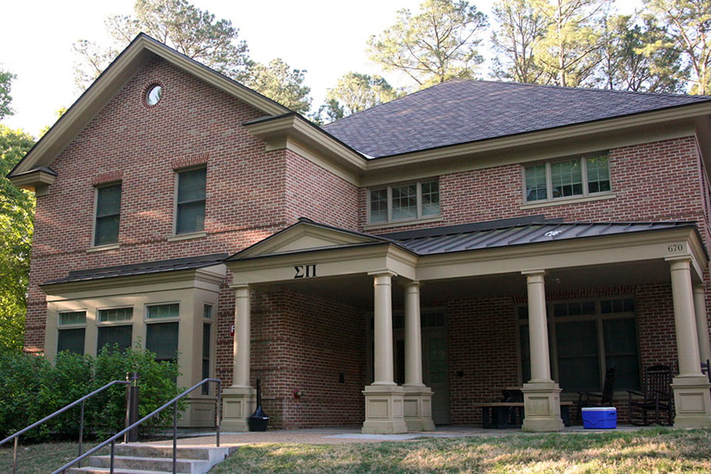 Brick fraternity house with a front porch and bushes