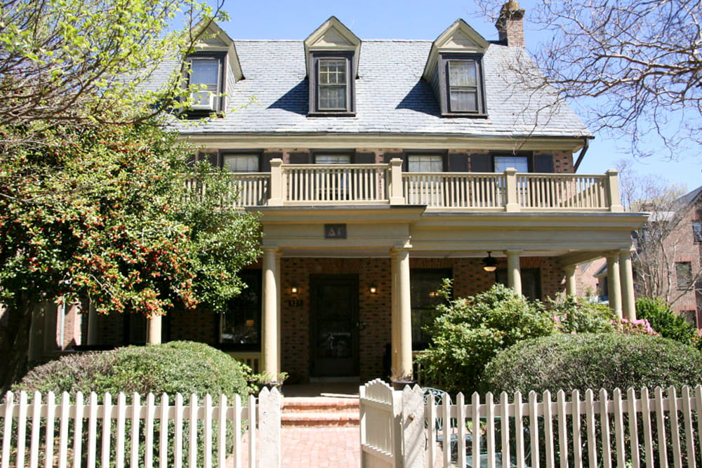 An historic brick house with dormer windows and double front porch and white picket fence