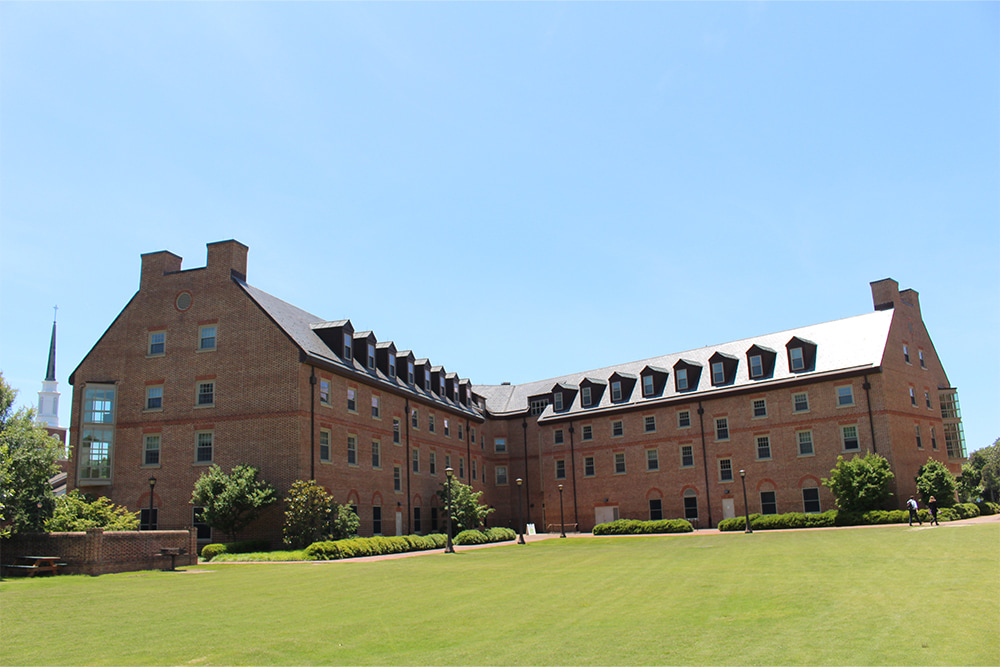 Brick, windowed dorm building surrounded by a vast green lawn.