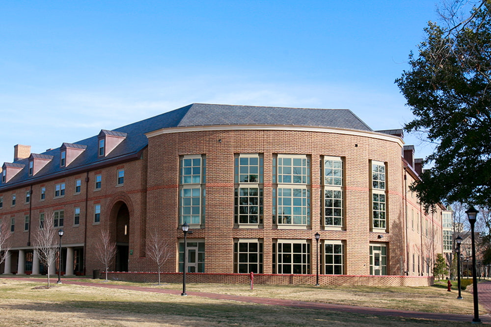 Brick dorm building with a large, windowed space surrounded by a vast green lawn.