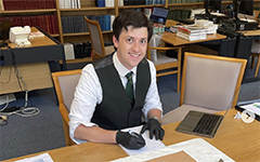 A student working at a desk with gloves smiling and examining a rare document