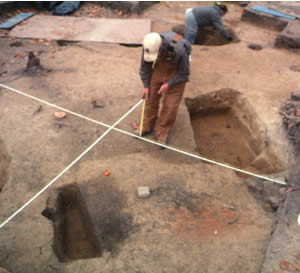 Excavation and mapping of subfloor pits. Most features are excavated in sections, allowing the archaeologists to examine and record profile views of the soil deposits.