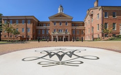 The brick exterior of the Alumni House with a large cypher on the driveway in front
