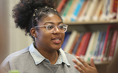 Student speaking in a conversation with a shelf of books behind