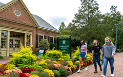 Three masked students walking past the Office of Undergraduate Admission building