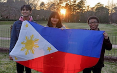 Three students pose in front of the Sunken Garden, holding up a Filipino flag.