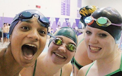 Three Tribe Swim club members, adorned with swim caps and goggles, smile before getting in the pool.