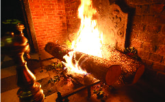 Yule logs burning in a large brick fireplace with sprigs of holly tossed around the logs