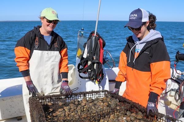 two students look at sea grass in boat on water