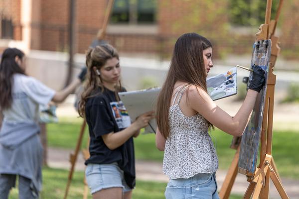 Three students standing outside in the spring painting on tall easels